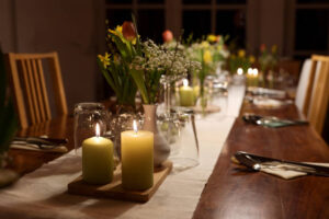 Table setting for a large dinner party with family and friends decorated with candles, spring flowers and various drinking glasses at night, selected focus, narrow depth of field