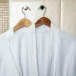 Two white rag bathrobes towels on wooden hangers in the interior of a stylish bathroom. Rest in otlele for two.